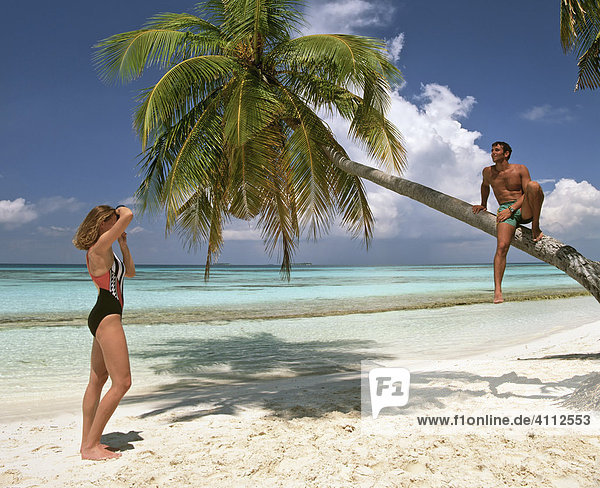 Junges Paar  Mann sitzt auf Palme  Fotografieren im Urlaub  Strand  Meer  Malediven