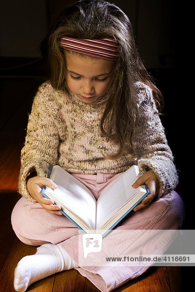 Lesendes kleines Mädchen im Schneidersitz