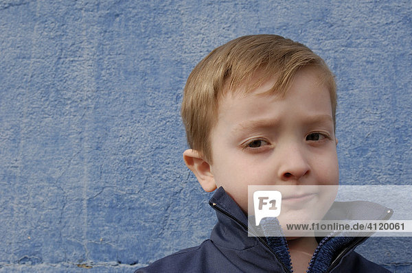 Young boy (age 5) standing against a blue wall