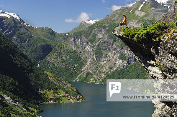Frau sitzt auf einer Felskanzel am Geiranger Fjord  Hellesylt  More og Romsdal  Norwegen