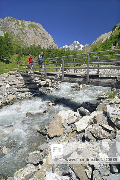 Hikers crossing a wooden bridge above a mountain stream  National Park Hohe Tauern  Tyrol  Austria