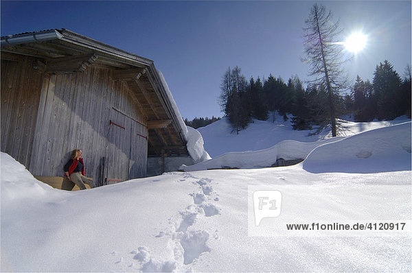 Eine Frau sitzt vor einem Holzschuppen in verschneiter Landschaft  Leutasch  Tirol  Österreich