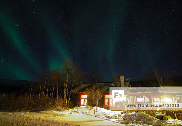 Beleuchtete Holzhütte Wohnhaus  verschneit mit Nordlichtern (Polarlicht  Aurora Borealis)  Finnmark  Nord Norwegen  Skandinavien