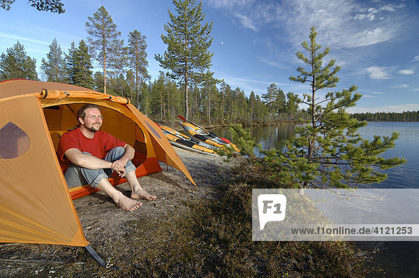 Mann sitzt vor einem Zelt am Seeufer  blickt in die Ferne Femundsmarka Nationalpark  Femundsmark  Norwegen