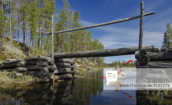 Frau paddelt auf einem Wasserkanal unter einer kleinen Holzbrücke durch  Femundsmarka Nationalpark  Femundsmark  Norwegen
