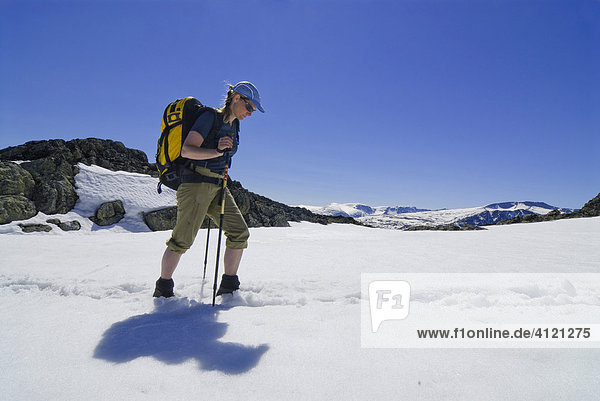 Frau mit Rucksack und Wanderstock stapft durch ein Schneefeld bei einer Bergtour  Jotunheimen Nationalpark  Vaga  Oppland  Norwegen
