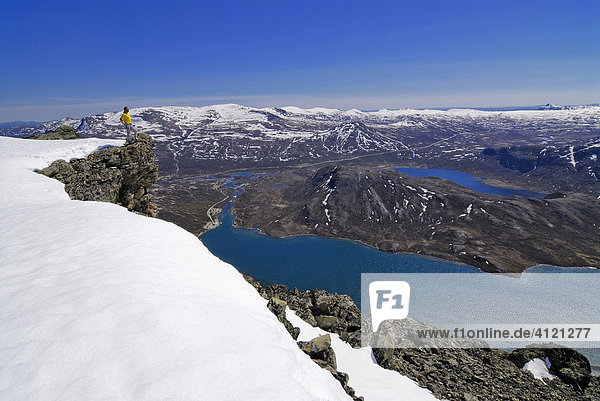 Hiker standing on a snow-covered rock pulpit looking over a vast landscape with mountains and lakes  Jotunheimen National Park  Vaga  Oppland  Norway