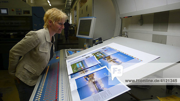 Blonde Frau kontrolliert die Druckqualität eines Druckbogens in der Druckerei beim Andruck eines Buchcovers