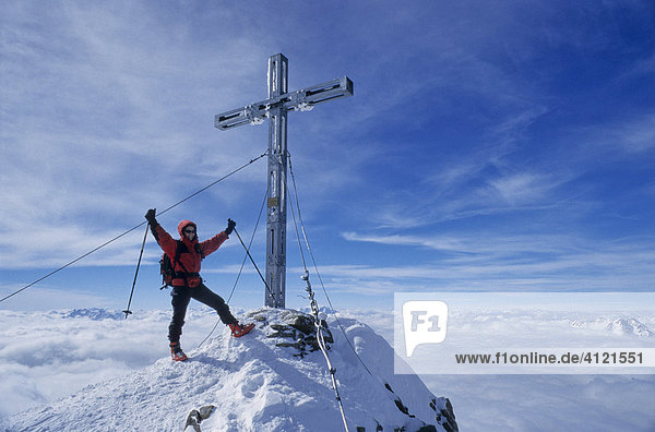 Bergsteigerin steht am Gipfel des Similaun neben dem eisernen Gipfelkreuz und streckt triumphal und siegesbewusst die Arme in den Himmel  Tirol  Österreich  Europa