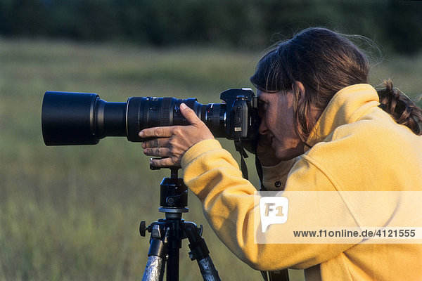 Female photographer wearing a yellow jacket  taking a picture with a camera  long lens  tripod