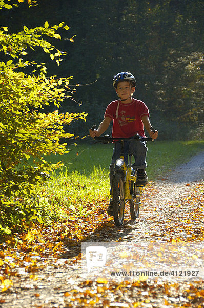 Kind fährt Rad auf einem Waldweg im Herbst