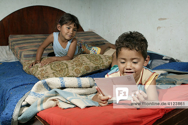 Guarani children sitting on the bed playing and reading in the poor area of Chacarita  Asuncion  Paraguay  South America
