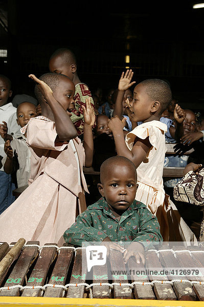 Young boy leaning on a marimba in front of two young girls dancing during a church service in Douala  Cameroon  Africa