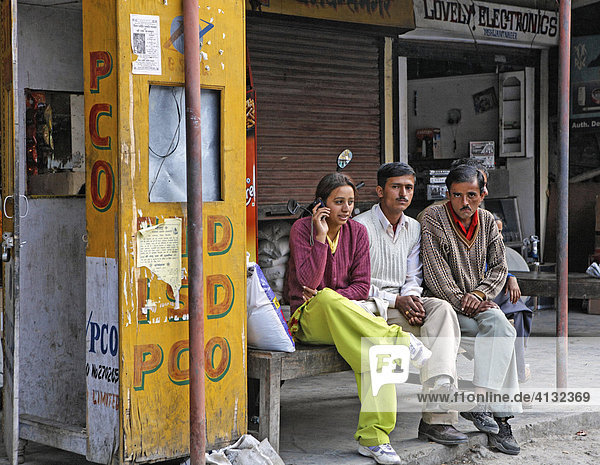 Eine Frau sitzt vor einer Telefonzelle und telefoniert mit ihrem Mobiltelefon  Maryog  Indien