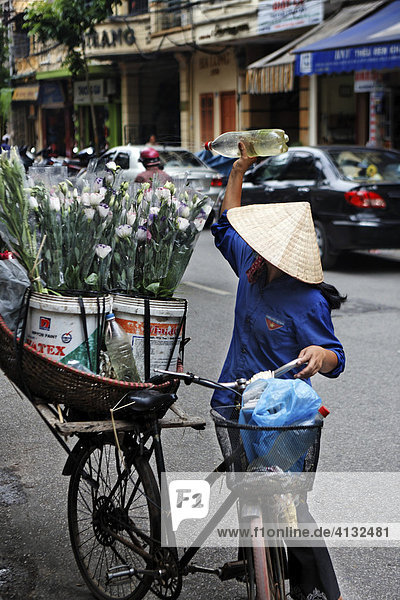 Frau giesst Blumen  die sie auf dem Gepäckträger ihres Fahrrads durch die Altstadt transportiert  Hanoi  Vietnam  Asien