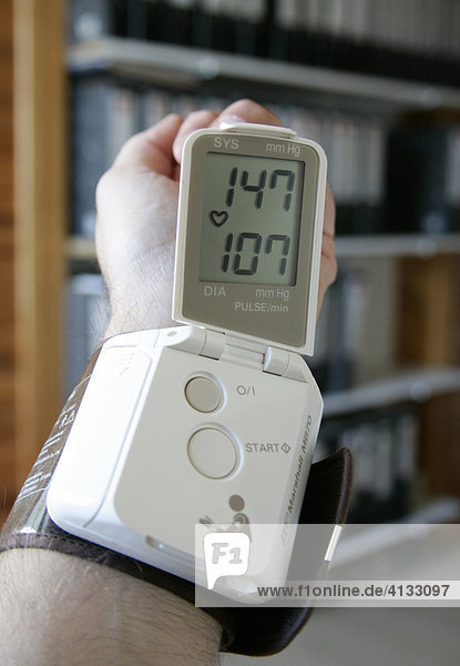 Wrist with blood pressure meter (sphygmomanometer) with office in the background