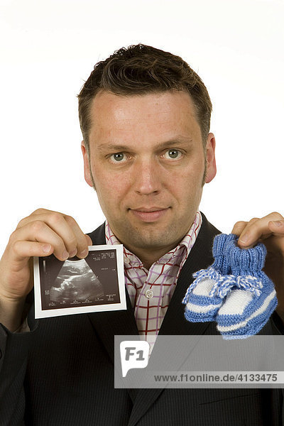 Geschäftsmann / Manager 40-jährig hält Babyschuhe und Ultraschallbild