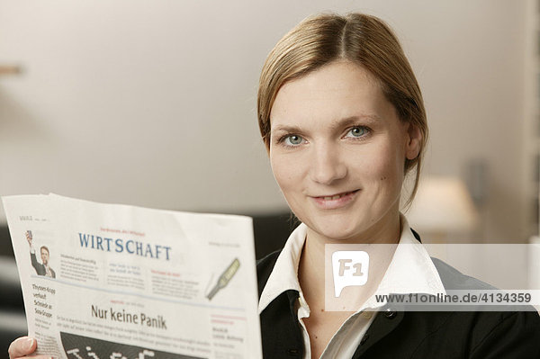 Junge blonde Frau mit Wirtschaftsteil einer Zeitung  lächelt