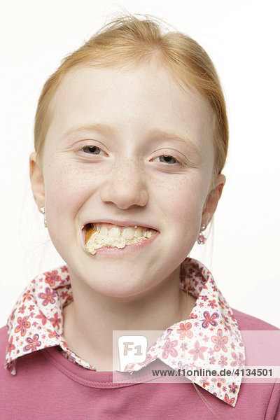 8-jähriges Mädchen mit roten Haaren mit Brot im Mund