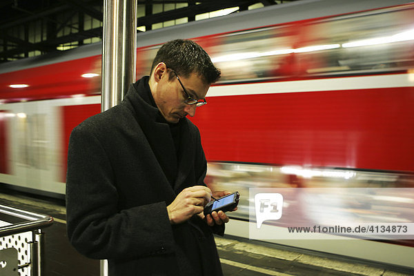 DEU Bundesrepublik Deutschland : Mann arbeitet mit seinem Pocket Computer PDA beim warten auf den Zug auf dem Bahnsteig.