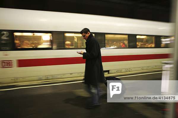 DEU Bundesrepublik Deutschland : Mann läuft mit seinem Handy und einem Koffer Trolley auf dem Bahnsteig.