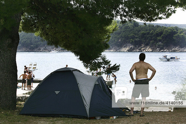 Man in front of his tent at Kovacine Campground  with its concrete beach  swimming  and boat docks  Cres Island  Croatia  Europe