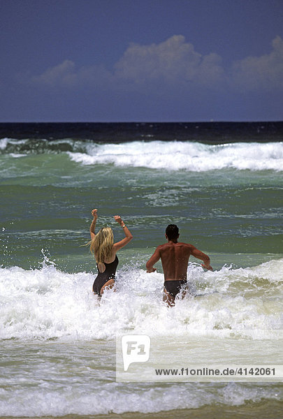 Couple jumping into the waves at Surfers Paradise Beach  Gold Coast  Queensland  Australia