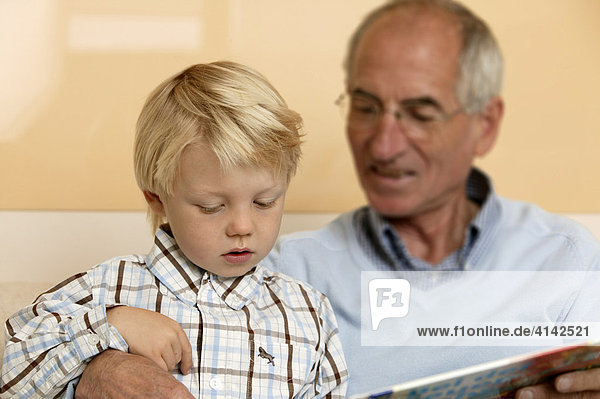 älterer Herr liest seinem Enkel aus einem Buch vor