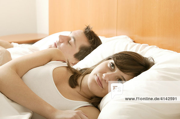 Young couple in bed  he sleeps  she is awake