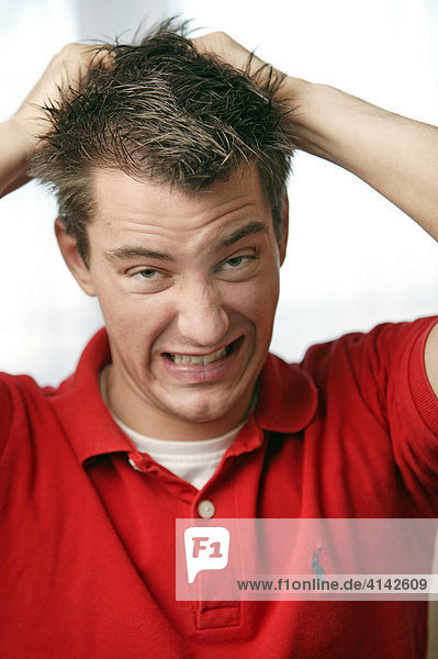 Young man in red sports shirt tears at his hair