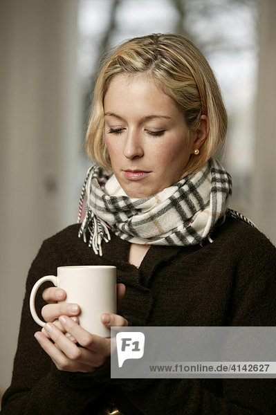 Junge Frau im dunklen Pullover mit Schal  mit Tasse