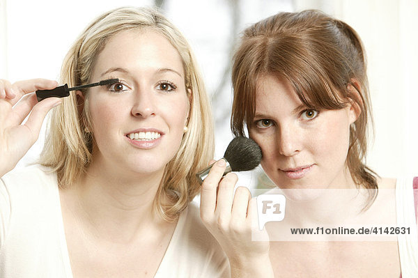 Two young women applying make-up
