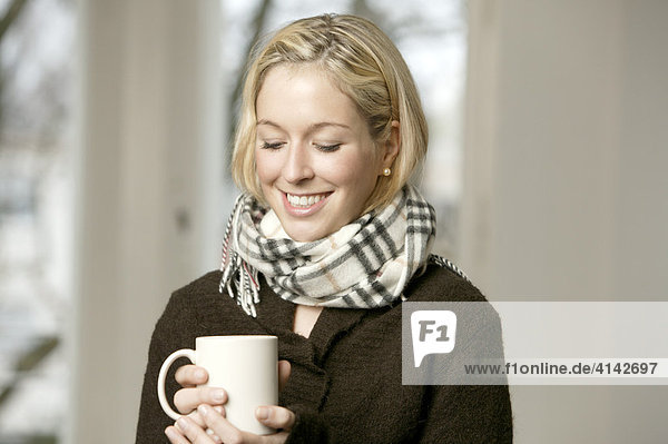 Junge Frau im dunklen Pullover mit Schal  mit Tasse  lächelt