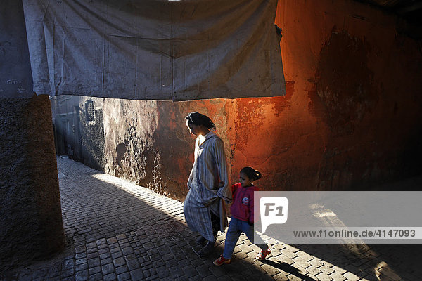 Frau mit Kind geht durch enge Gasse mit Sonnensegel  historische Medina  Marrakesch  Marokko  Afrika