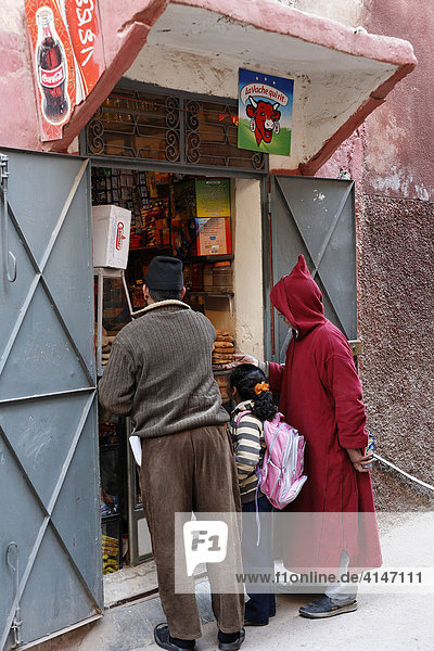 Young girl carrying school backpack standing between two men in front of a typical small food kiosk  Marrakesh  Morocco  Africa