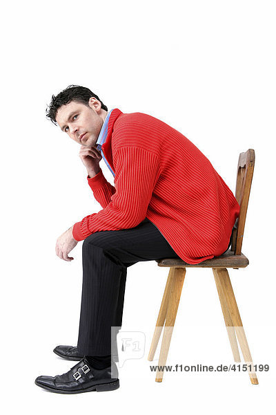 Man wearing red jacket sitting on an old wooden chair