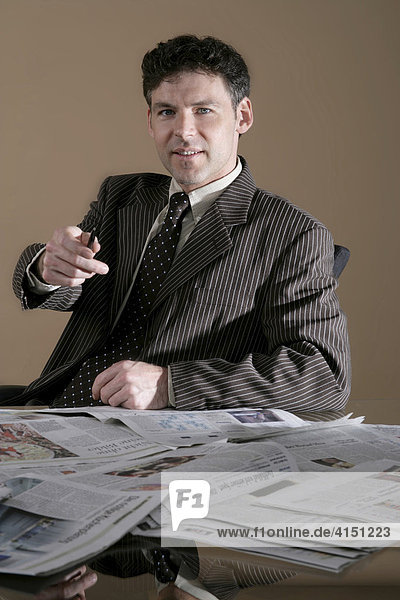 Businessman sitting at a desk covered in newspapers
