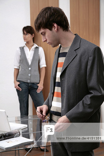 Young man standing at a desk  young woman standing in background