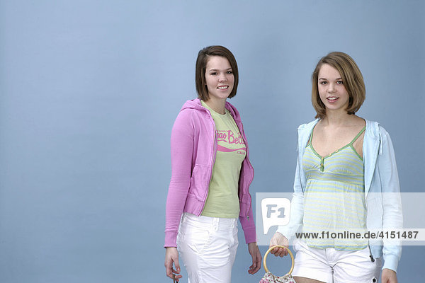 Two girls wearing casual outfits strolling in front of a light blue backdrop