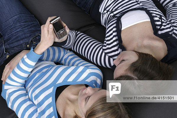 Zwei Mädchen liegen auf großem Kissen und versenden SMS