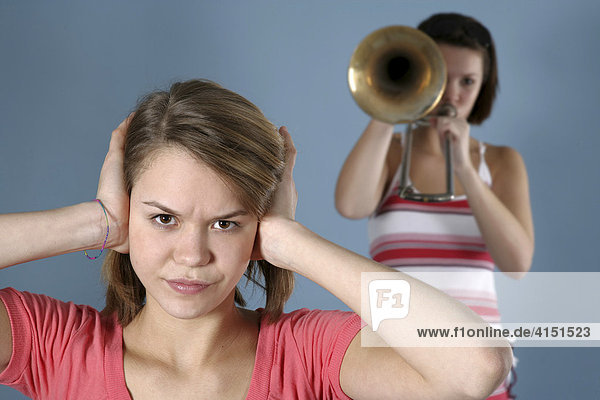 Girl practicing her trombone while her friend covers her ears  annoyed