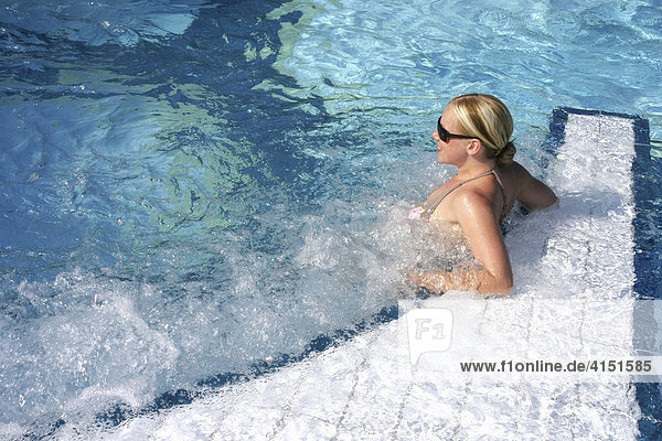 Junge Frau lehnt am Beckenrand eines Schwimmbades