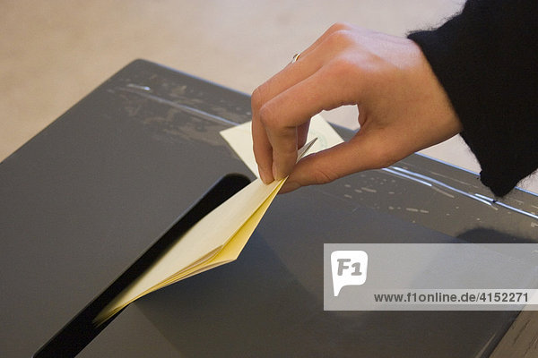 Hand wirft Wahlzettel in eine Wahlurne