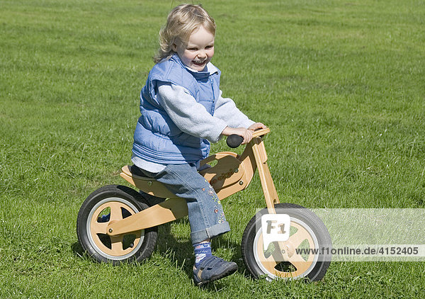 Kleines Mädchen fährt mit ihrem Laufrad über eine Wiese