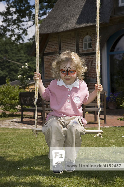 Little girl with a make up butterfly on her face sitting on a swing