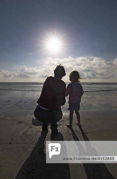 Young woman and her little daughter cowering at the beach and looking over the sea  Denmark