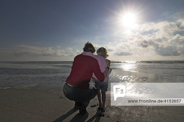 Junge Frau und ihre kleine Tochter hocken am Strand und schauen auf das Meer  Dänemark