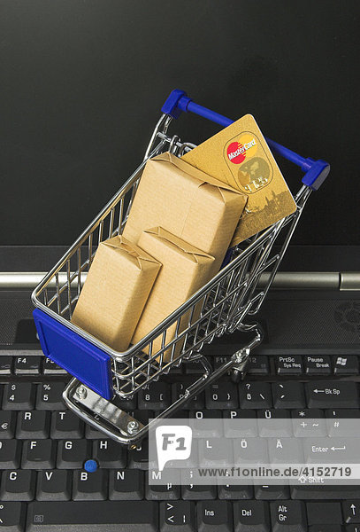 Einkaufen im Internet  ein Einkaufswagen mit Paketen und einer Kreditkarte steht auf der Tastatur eines Notebook Computers