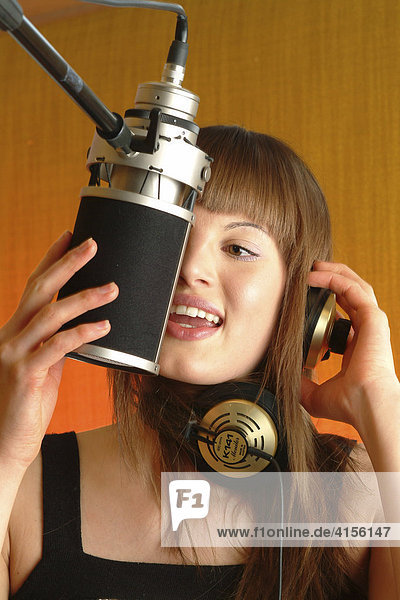 Junge Frau mit Kopfhörer singt in das Mikrofon eines Tonstudios