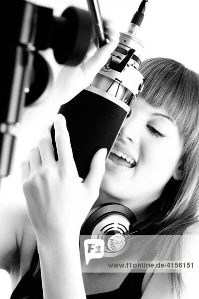 Junge Frau mit Kopfhörer singt mit Gefühl in das Mikrofon eines Tonstudios